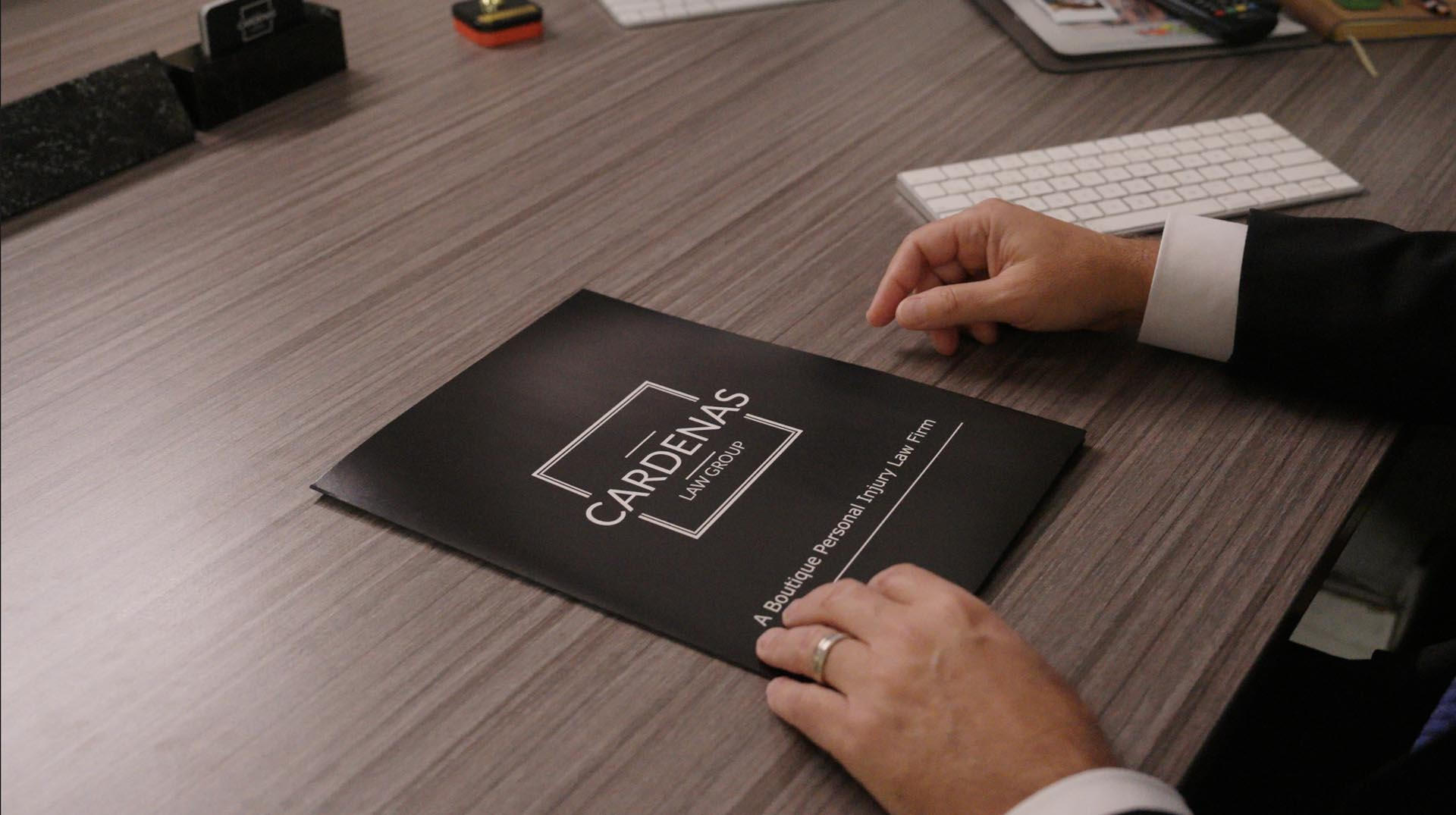 Hands resting on a folder labeled "Cardenas" on a wooden desk
